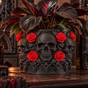 May include: A matte black cylindrical planter featuring a relief design of multiple human skulls interspersed with vibrant red roses and green leaves. The base of the planter is decorated with a repeating gothic arch pattern in black.