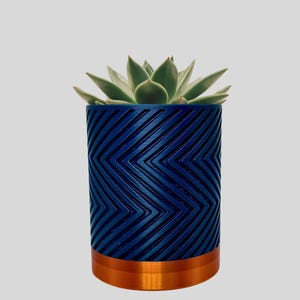 May include: A blue planter with a chevron pattern and a copper rim. The planter is filled with a succulent plant.