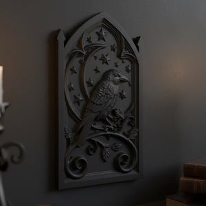 May include: A dark grey wall plaque with a detailed relief of a raven perched on a branch, surrounded by stars and a crescent moon. The gothic-style artwork is mounted on a dark grey wall, with a lit candle in the foreground.