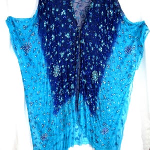 May include: A sheer, open-front kaftan featuring an ombre color transition from deep navy blue at the top to bright turquoise at the hem. The garment is adorned with intricate silver beadwork, sequins, and floral embroidery throughout the fabric.