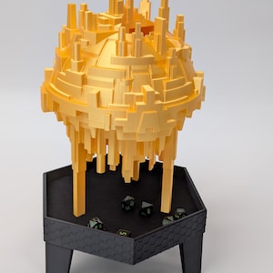 May include: A gold-colored, 3D-printed tabletop gaming accessory. The spherical structure, resembling a futuristic city, sits atop a black hexagonal tray with dice. The tray is supported by three black legs.