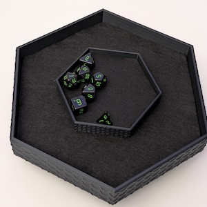 Op de afbeelding: Zwarte zeshoekige dobbelsteenbak met een kleinere zeshoekige bak erin. De bak is gevuld met zwarte dobbelstenen met groene nummers. De dobbelstenen tonen de nummers 1, 2, 3, 4, 5, 6, 7, 8, 9 en 10.