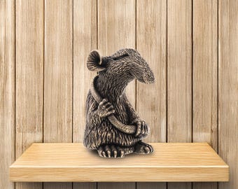 May include: A bronze figurine of a mouse holding a snake in its paws. The mouse is sitting on a wooden shelf.