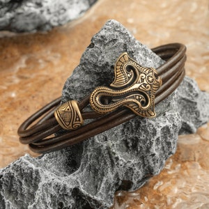 May include: A brown leather bracelet with a decorative gold-tone metal clasp. The clasp features an intricate design with a floral motif.