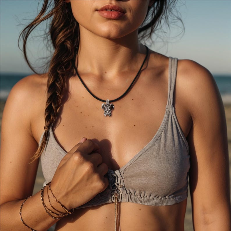 May include: A silver turtle pendant necklace on a black cord. The pendant features detailed patterns. The necklace is a piece of jewellery and is worn around the neck.