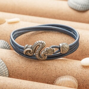 May include: A blue leather bracelet with a silver snake charm and a silver bead with a geometric design.