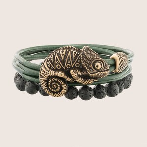 Op de afbeelding: Een groene leren armband met zwarte lavastenen en een gouden kameleonbedel. De bedel heeft ingewikkelde details en een getextureerd oppervlak.