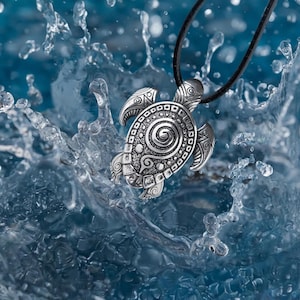 May include: A silver turtle pendant necklace with detailed patterns, set against a backdrop of splashing water. The pendant is attached to a black cord, featuring a detailed design of the turtle's shell and head. The water creates a dynamic and aquatic theme.