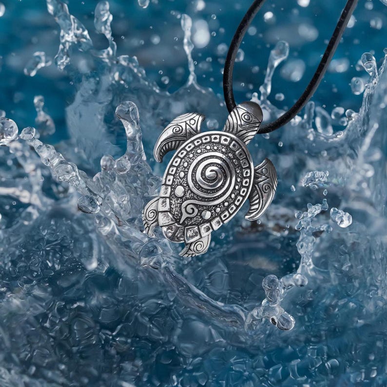 May include: A silver turtle pendant necklace with detailed patterns, set against a backdrop of splashing water. The pendant is attached to a black cord, featuring a detailed design of the turtle's shell and head. The water creates a dynamic and aquatic theme.