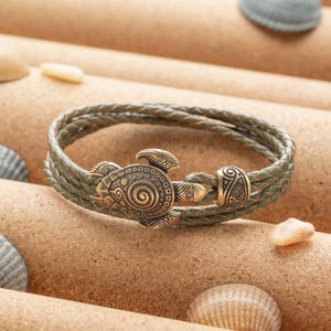 May include: A green leather bracelet with a gold-toned turtle charm. The turtle has intricate details and a spiral design.