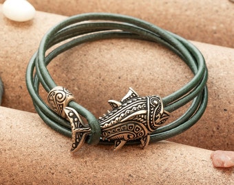 May include: A green leather bracelet with a detailed fish charm. The charm is made of metal and has a gold finish.