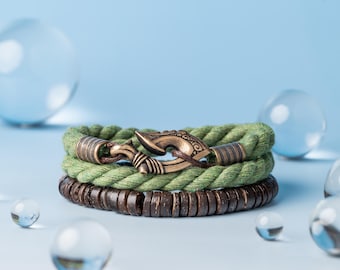May include: A set of three bracelets featuring a green rope with a brown wooden bead bracelet and a bronze hook clasp.