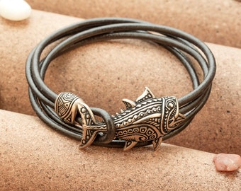 May include: A brown leather bracelet with a decorative fish charm. The charm is made of metal and has a detailed design.