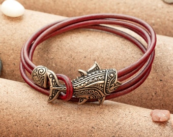 May include: A red leather bracelet with a silver fish charm. The fish charm has intricate details and a textured surface.