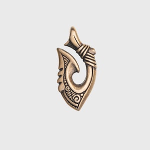 May include: A gold-colored metal pendant shaped like a traditional Hawaiian fish hook, known as a "hei"