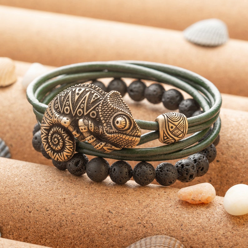 Op de afbeelding: Een groene leren armband met zwarte lavastenen en een gouden kameleonbedel.