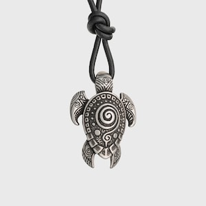 May include: A silver turtle pendant with detailed spiral and dot patterns, hanging from a black leather cord. The pendant's shell and flippers are adorned with intricate designs, giving it a textured look. The cord is knotted.