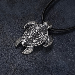 May include: Silver turtle pendant necklace. The pendant has detailed patterns and a spiral design on the shell. The necklace has a black cord. The turtle pendant is a symbol of longevity and wisdom.