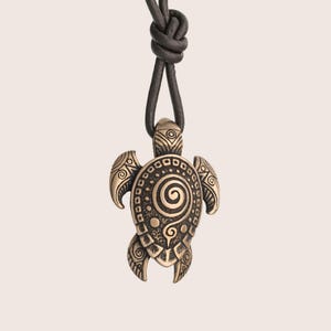 May include: Bronze turtle pendant necklace with a spiral design on a black leather cord. The turtle pendant has detailed patterns on its flippers and shell. The cord is knotted at the top.