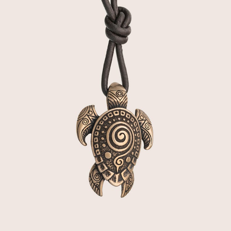 May include: Bronze turtle pendant necklace with a spiral design on a black leather cord. The turtle pendant has detailed patterns on its flippers and shell. The cord is knotted at the top.