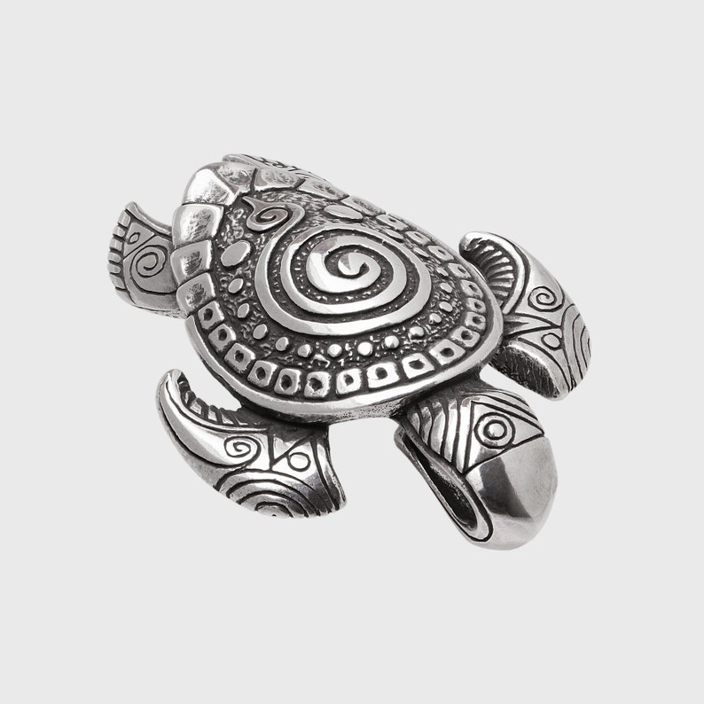 May include: A silver-coloured turtle figurine with detailed carvings. The shell features a spiral design and other intricate patterns. The flippers and head also have detailed carvings. The figurine is set against a plain background.