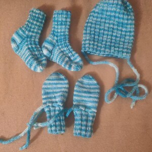 May include: A baby's knitted set in blue and white. The set comprises two pairs of socks, a beanie hat with ties, and a pair of mittens. The items are handmade with a striped pattern.