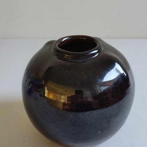 Może przedstawiać: Brązowy ceramiczny wazon o zaokrąglonym kształcie i gładkim, błyszczącym wykończeniu.