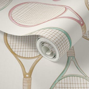 May include: Wallpaper roll featuring a repeating pattern of watercolor tennis rackets in pastel colors. The rackets have pink, green, and tan frames with beige netting, set against a cream background. The roll is partially unrolled.