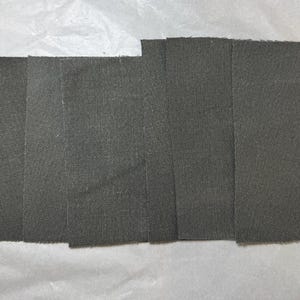 Puede incluir: Cinco muestras de tela gris oscuro dispuestas una al lado de la otra sobre una superficie blanca.