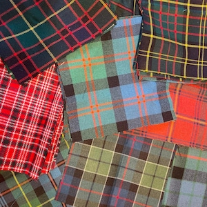May include: Assortment of colorful plaid fabric swatches in various colors, including red, green, blue, and yellow. The fabric has a classic tartan pattern, with intersecting horizontal and vertical lines.