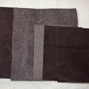 Puede incluir: Una colección de muestras de tela en varios tonos de marrón y gris. Las muestras rectangulares presentan diferentes texturas, incluyendo espiga y tejidos lisos. La disposición muestra una gama de tonos neutros adecuados para proyectos textiles.