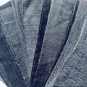 Może przedstawiać: Kolekcja próbek tkaniny dżinsowej w różnych odcieniach niebieskiego, ułożonych w kształt wachlarza. Próbki są zszyte ze sobą wzdłuż krawędzi, tworząc fakturowany i warstwowy efekt.