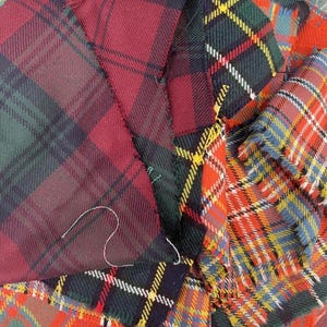 May include: Close-up of three different plaid fabrics in red, green, blue, and yellow. The fabrics are woven with a tartan pattern.