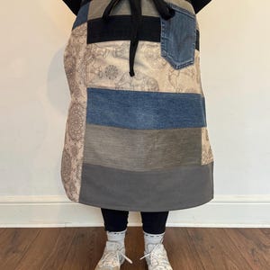 以下が含まれることがあります： デニムと他の生地で作られたパッチワークエプロン。エプロンは前面に大きなポケットとウエストにリボンが付いています。