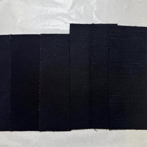 May include: Five black fabric swatches lined up side by side. The swatches are different shades of black.