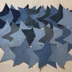 Puede incluir: Una colección de estrellas de mezclilla azul de varios tamaños, dispuestas en un racimo. Las estrellas están hechas de tela de mezclilla y tienen un aspecto ligeramente desgastado.