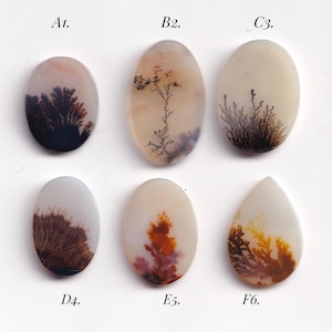 May include: Six polished dendritic agate gemstones in oval and teardrop shapes. The stones display unique patterns resembling trees and ferns in shades of brown, black, and orange against a translucent background. These stones are ideal for jewelry making.