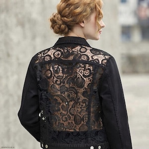 May include: A black jacket featuring a solid collar and long sleeves with a prominent back panel made of intricate black lace. The lace displays a detailed floral and circular pattern, while the jacket includes a buttoned hem and cuffs.