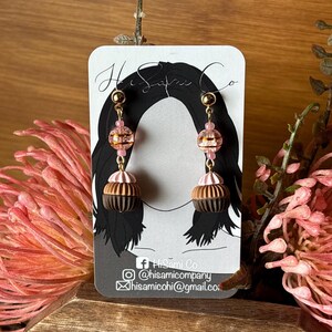 May include: A pair of dangle earrings with a brown and pink cupcake design. The earrings are made with glass beads and gold-toned metal.