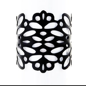 May include: Black leather bracelet with a cut-out design. The bracelet has a delicate, intricate pattern.