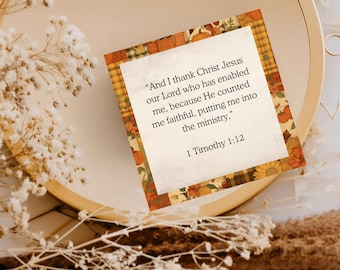 May include: A square card with a quote from 1 Timothy 1:12, featuring a decorative border with pumpkins and sunflowers. The card is set on a neutral background with dried flowers and a wooden hoop.