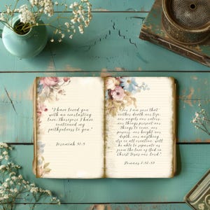 May include: An open book with lined pages, decorated with floral designs in pink, blue, and cream. The left page has a quote from Jeremiah 31:3, and the right page has a quote from Romans 8:38-39. The book is on a teal wooden surface.