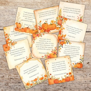 Pode incluir: Uma coleção de cartões quadrados com designs de outono. Cada cartão apresenta um versículo bíblico, abóboras e folhagens de outono em tons de laranja, amarelo e castanho. Os cartões estão dispostos sobre uma superfície de madeira.