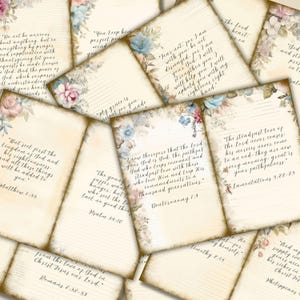 Op de afbeelding: Een verzameling vintage papieren kaarten met bloemaccenten in roze, blauw en cr&egrave;me. Elke kaart bevat handgeschreven tekst met religieuze citaten. De kaarten hebben een verouderde uitstraling.