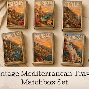 May include: A set of six rectangular matchboxes featuring vintage-style illustrations of Spain, Morocco, Italy, Montenegro, Monaco, and Greece. Each box displays a scenic coastal landscape at sunset with vibrant flowers and architectural details.