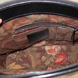 May include: Open view of a black leather handbag interior. The inside features a floral fabric lining with red and pink flowers, green leaves, and a brown background. There are several pockets and a zippered compartment.