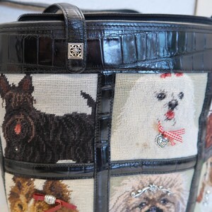May include: Black tote bag with a tapestry design featuring various dog breeds. The bag has a black leather handle and trim, with a silver-colored decorative clasp. The tapestry panels showcase different dog portraits.