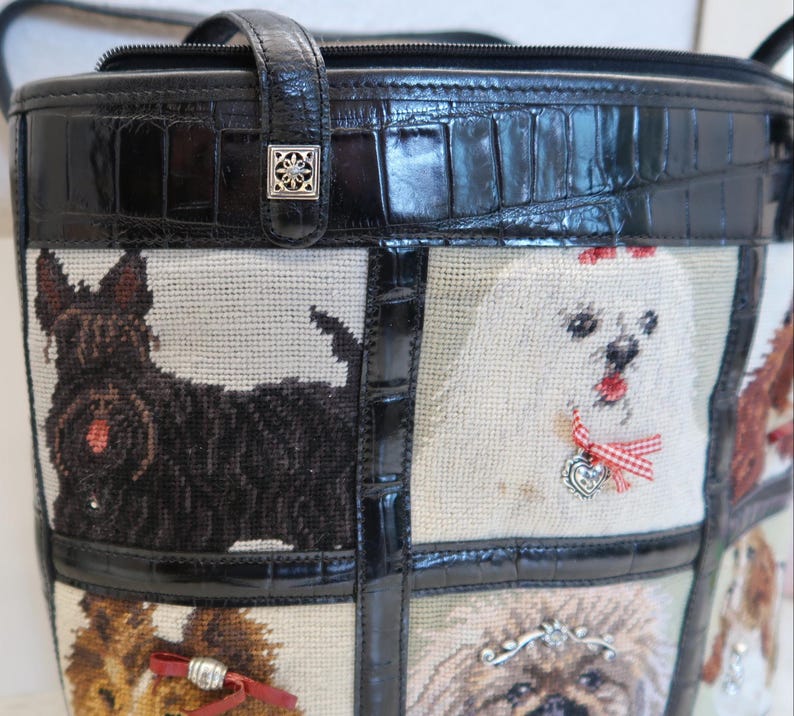 May include: Black tote bag with a tapestry design featuring various dog breeds. The bag has a black leather handle and trim, with a silver-colored decorative clasp. The tapestry panels showcase different dog portraits.