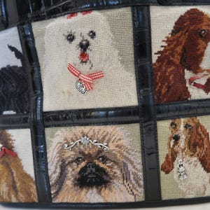 May include: A tapestry tote bag featuring various dog breeds. The bag has a black leather trim and handles. The tapestry panels depict different dogs, including a white dog with a red bow, and a brown and white dog.
