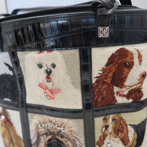 May include: A black tote bag with a stitched dog design. The bag features a black crocodile-embossed leather top and trim. The dog portraits are on a beige background, with red bows and silver embellishments.